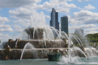 Photo of a fountain with water shooting up in arcs, and two glass skyscrapers in the background