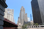 Photo of a bridge in the foregound left, a glassed building in the foreground right and a tall masonry building in the background