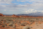 Photo of sparse green vegetation in the foreground, red rock formations in the middle and mountains in the background 