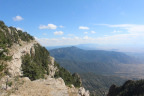 Photo of a cliff with trees on it in the foreground and mountain ranges in the background