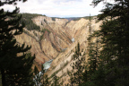 Photo of the Yellowstone River with brown hills on either side and dark pines in the foregound 