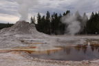 Photo of a cone with steam rising and a hot spring next to it with brown edges
